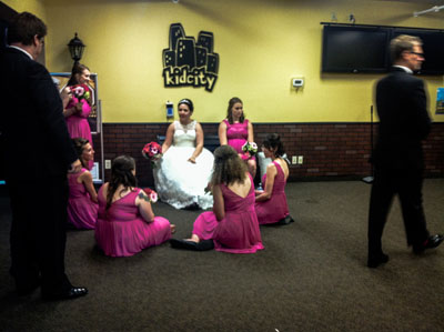 Candid wedding scene captured by Justin Adelmann, featuring the bride surrounded by bridesmaids in pink dresses, preparing for the ceremony in a casual setting.