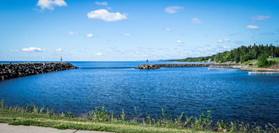 Scenic view of a tranquil lake bordered by a rocky breakwater under a clear blue sky, photographed by Justin Adelmann.