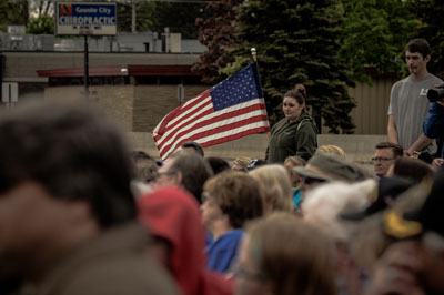 A woman standing in a crowd, holding an American flag.